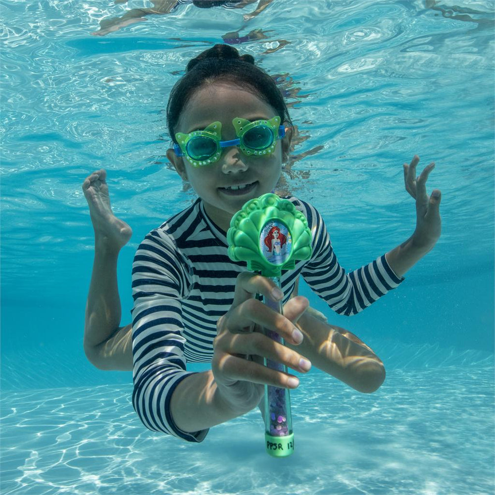Child underwater in a pool holding a green Ariel dive wand, wearing striped swim shirt and goggles.