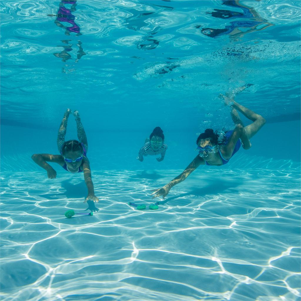 Children swimming underwater in a pool with clear blue water retrieving dive wands.